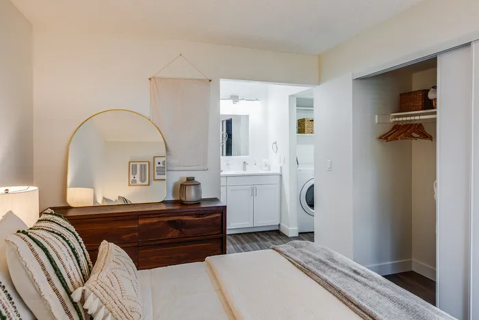 Chic bedroom with decorative pillows, rustic wooden dresser, and attached modern bathroom with laundry area.