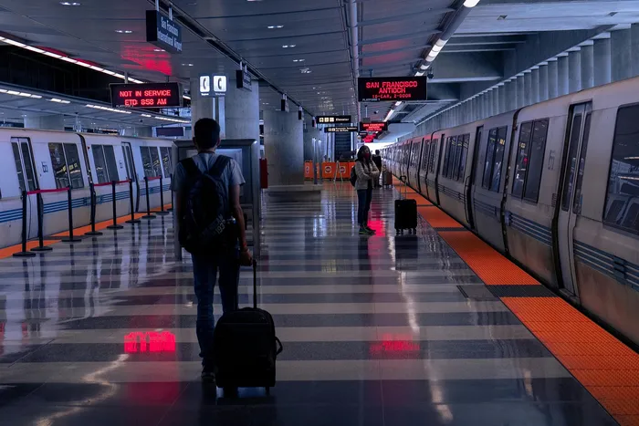 Modern transit station with sleek silver train, reflective flooring, and travelers with luggage anticipating their journey.