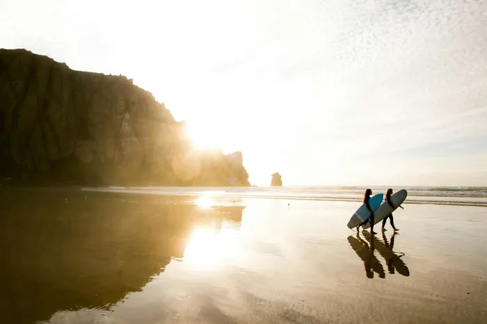 Breathtaking beach sunrise scene with surfers walking along the serene shoreline, backlit by the radiant sun.