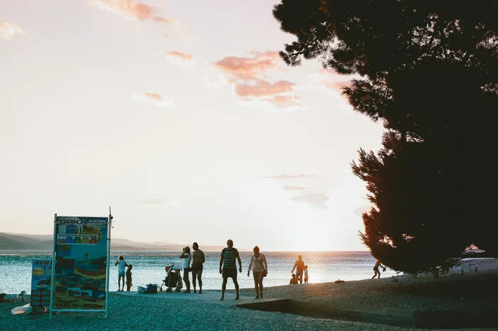 Serene beach scene at sunset with people enjoying the coastline and water activities, highlighted by a vibrant sky and gentle waves.