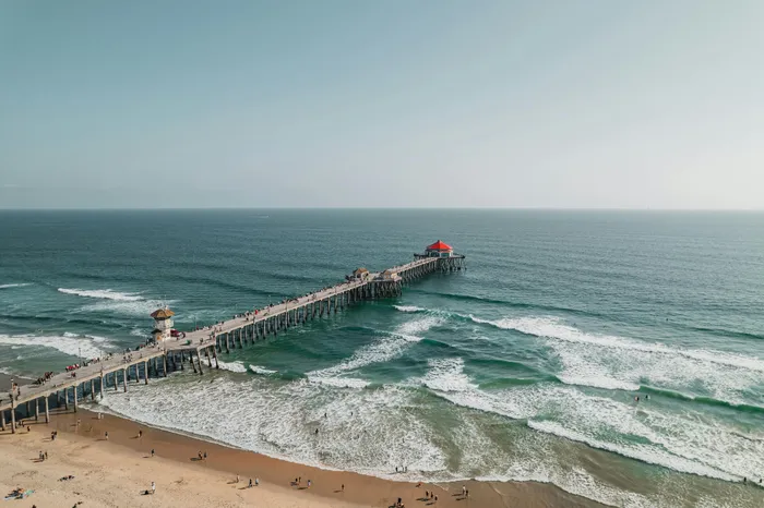 Stunning coastal view featuring a long pier extending into the ocean, with waves gently crashing onto the sandy beach below, ideal for relaxation and beach activities.