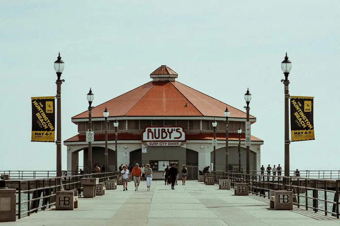 Charming diner with a red roof at the end of a bustling pier, surrounded by lamp posts and festive banners.