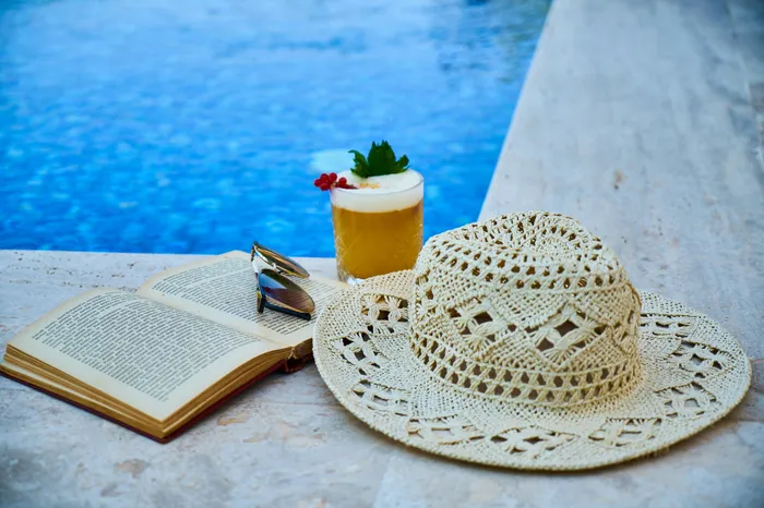 Inviting poolside scene with a refreshing cocktail, a straw hat, sunglasses, and an open book, perfect for relaxation and leisure.