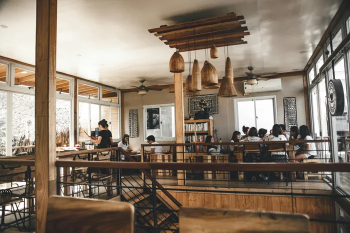 Charming and cozy caf&eacute; interior with stylish wooden decor, featuring large windows, a group of people enjoying coffee, warm lighting, and an inviting atmosphere.