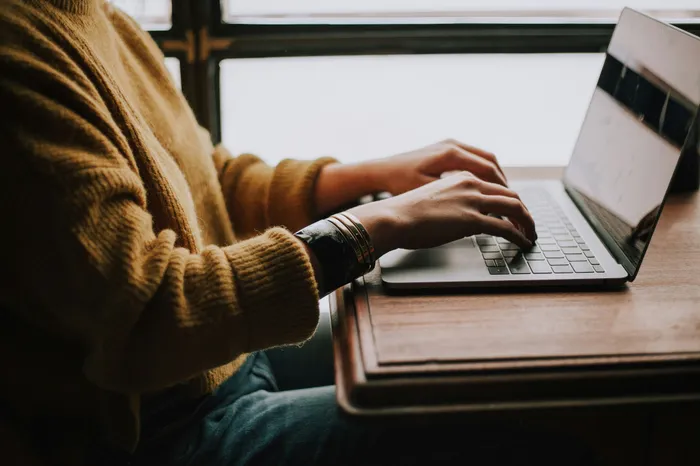 Cozy and stylish workspace with a person typing on a sleek laptop at a wooden desk.