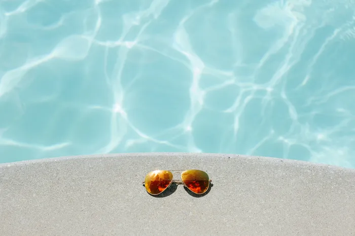 Gleaming aviator sunglasses resting elegantly on the edge of a shimmering pool, inviting relaxation under the sun.