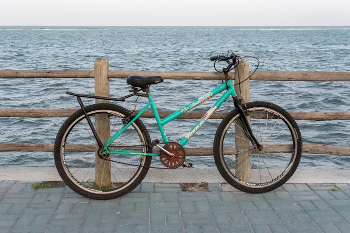 Vibrant turquoise bicycle parked by a scenic seaside boardwalk, showcasing serene ocean views and a rustic wooden fence.