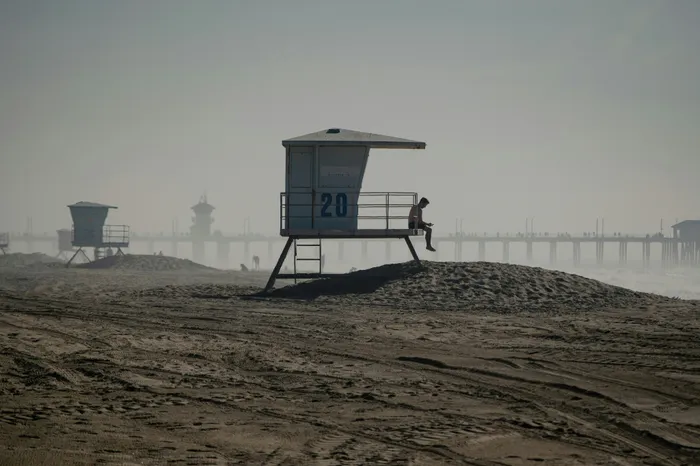 Serene coastal scene with lifeguard tower, sandy beach, and misty pier backdrop.