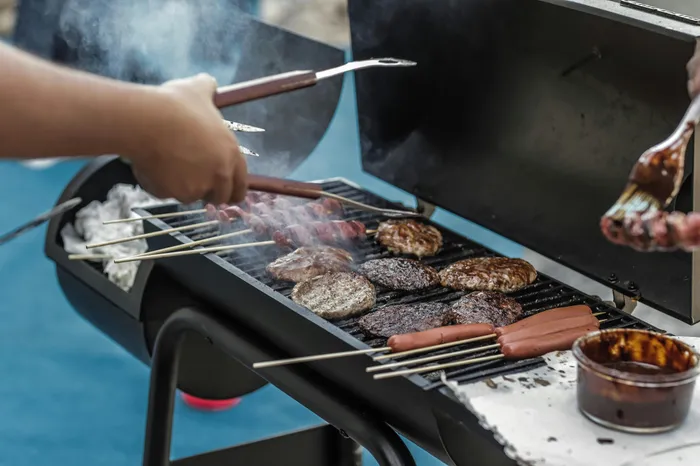Inviting outdoor barbecue scene with sizzling burgers, skewers, and hot dogs on a grill, perfect for summer gatherings.