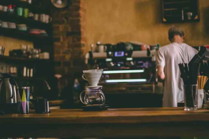 Cozy coffee shop ambiance with rustic wooden counter, pour-over setup, and barista in the background.