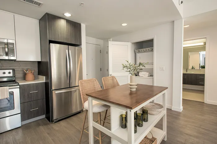 Modern kitchen with sleek stainless steel appliances, stylish wood flooring, and cozy dining area with woven chairs and a tasteful centerpiece.