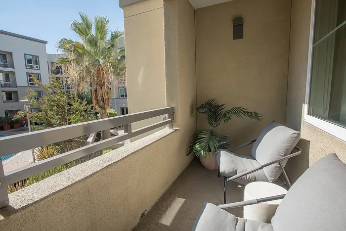 Charming balcony with cozy seating, offering a serene view of lush greenery and palm trees under a bright sky.