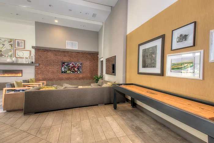 Modern living room with stylish brick accent wall, cozy fireplace, wall art, and large plush sofas. Features an inviting entertainment area with a TV and a sleek shuffleboard table, perfect for relaxation and social gatherings.