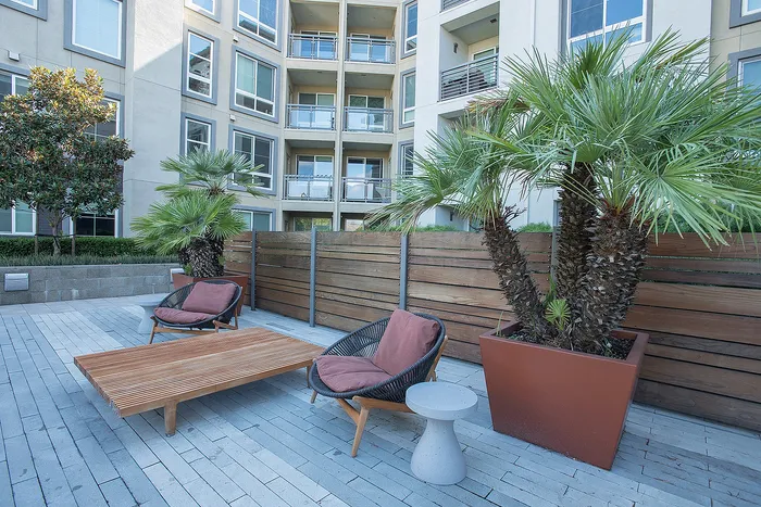 Chic outdoor patio with modern seating, lush palm trees, and a luxurious apartment backdrop.