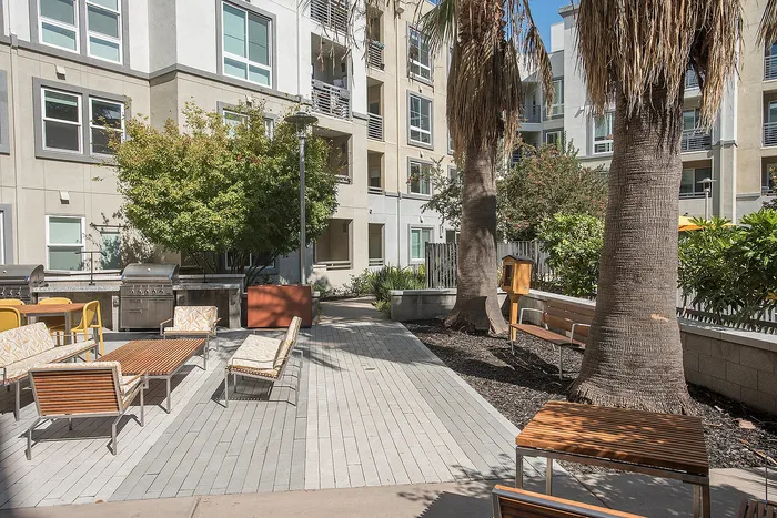 Inviting apartment courtyard featuring stylish outdoor seating, lush greenery, and modern barbecue facilities.
