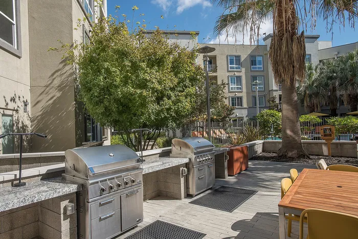Modern outdoor patio with sleek stainless steel BBQ grills, surrounded by lush greenery and inviting dining area, perfect for sunny gatherings.