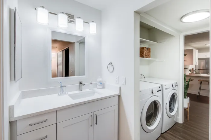 Elegant bathroom with modern vanity and integrated laundry area, featuring sleek washer and dryer in a sophisticated apartment setting.