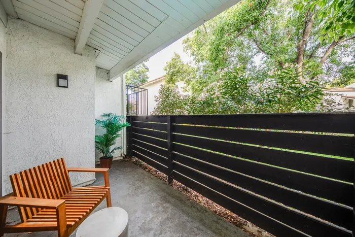 Charming outdoor patio with stylish wooden seating, lush greenery, and a modern privacy fence offering a serene retreat.