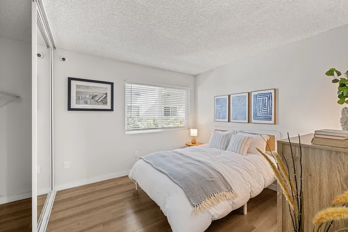 Bright and cozy bedroom with modern decor, wooden flooring, and large window allowing ample natural light.