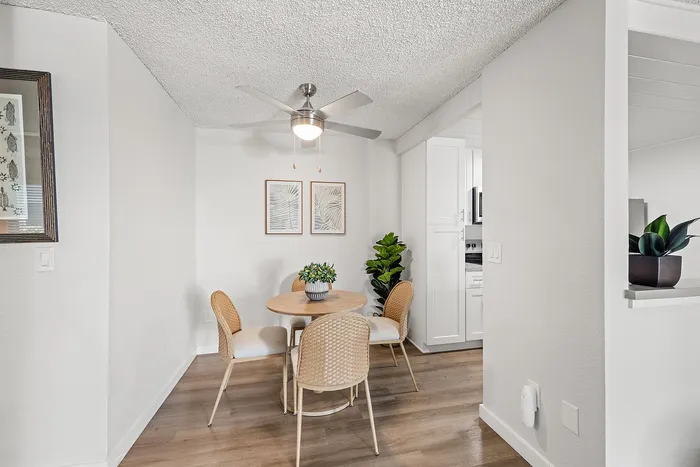 Charming dining nook with modern round table, cozy wicker chairs, and lush greenery, adjacent to a bright, contemporary kitchen.