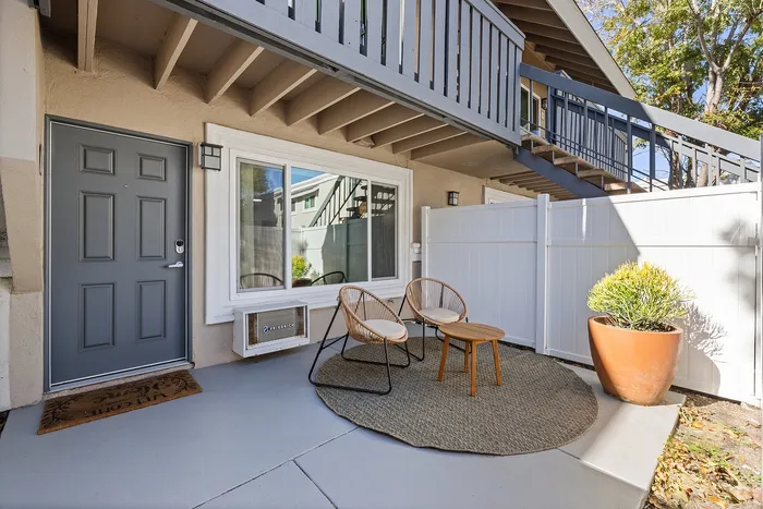 Inviting apartment entrance with chic patio seating, modern gray door, and potted greenery.