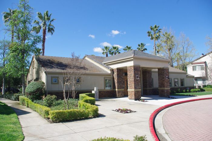 Twin Creeks clubhouse exterior with a covered entryway, tile roof, and palm-lined driveway.