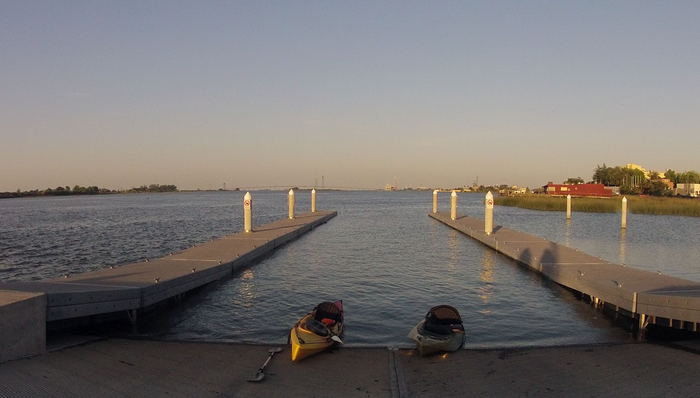 Sunset view down empty marina docks on the water near Antioch, with kayaks resting on the shore.