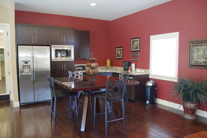 Twin Creeks clubhouse kitchen with stainless steel refrigerator, dark cabinetry, and a dining table with bar-style seating.