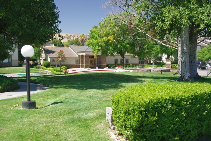 Twin Creeks landscaped grounds with mature trees, a lamppost, and lush green lawn leading toward the community buildings.