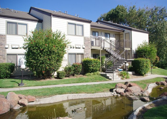 Twin Creeks apartment building exterior with private balconies and stairways overlooking a rock-lined pond.