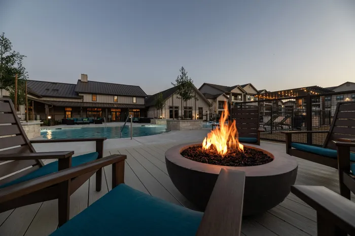 Luxurious outdoor patio with cozy fire pit overlooking a sparkling pool and modern apartment buildings at sunset.