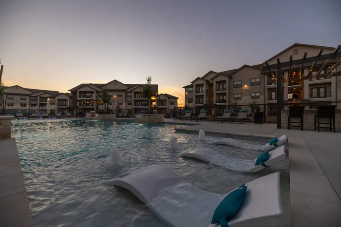 Luxurious apartment complex at sunset with a pristine pool, relaxing lounge chairs, and modern architecture.