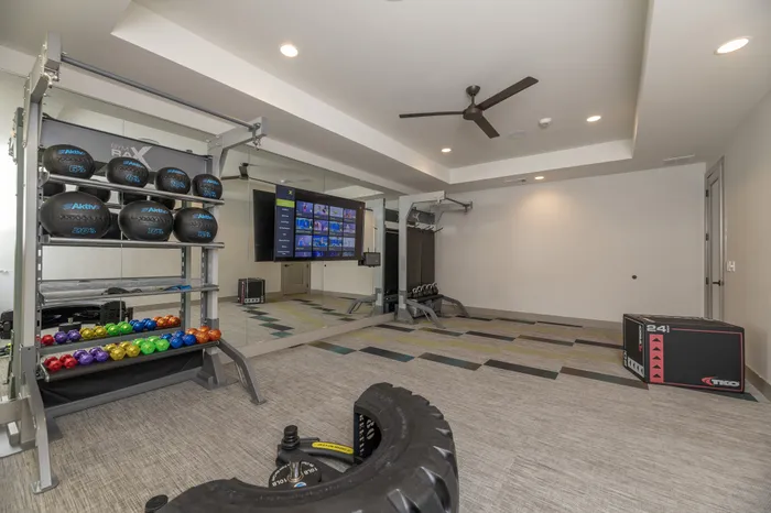 Modern home gym equipped with kettlebells, medicine balls, and fitness equipment, featuring a large wall-mounted TV for virtual workouts.