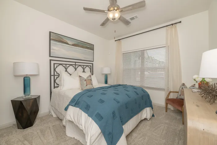Elegant bedroom featuring a plush bed with a modern headboard, blue accents, textured carpet, and ambient lighting.