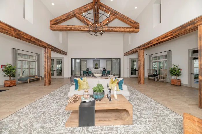 Elegant modern living room with high ceilings, exposed wooden beams, and chic decor featuring a stylish chandelier and abundant natural light.