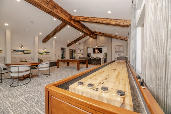 Inviting clubhouse lounge featuring a shuffleboard table, modern seating, and rustic exposed beams.