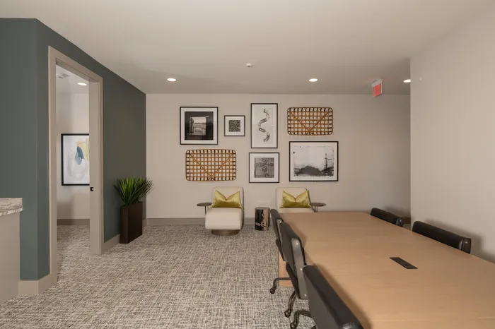 Modern apartment lounge with chic decor, featuring stylish art, comfortable seating, and a sleek conference table.