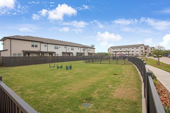 Inviting residential community with modern townhomes and expansive green space, perfect for relaxation and play under a clear blue sky.