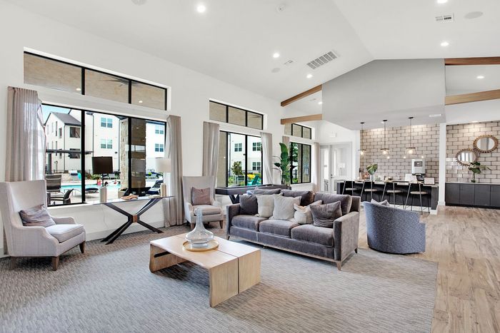 Luxurious open-plan living area featuring a chic lounge, stylish kitchen with bar seating, and expansive windows with pool view.
