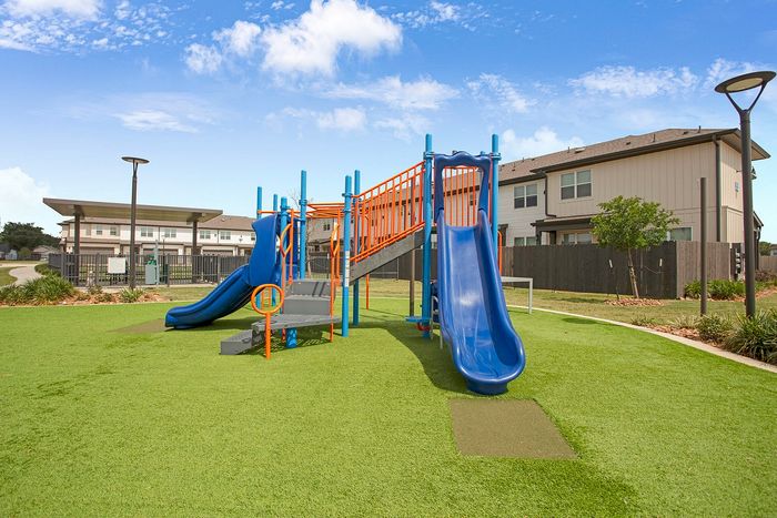 Vibrant outdoor playground with blue and orange slides set on lush green grass, perfect for family living in a welcoming neighborhood.