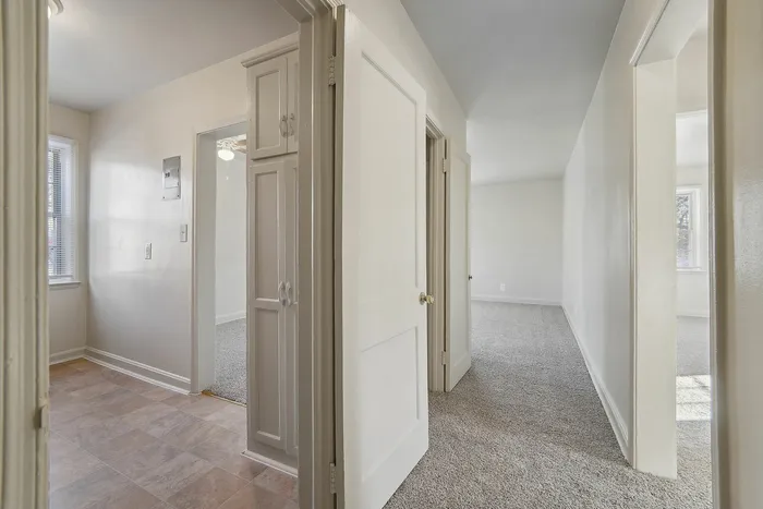 Bright hallway view with doorways leading to carpeted and tiled floors in a modern apartment.