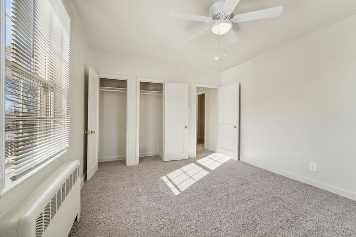 Sunlit bedroom with plush carpeting, white closet doors, and ceiling fan.