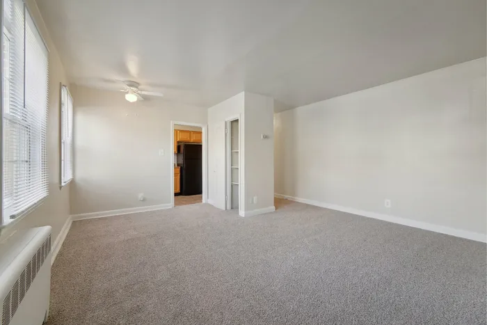 Spacious living room with light gray carpet, ceiling fan, and adjoining kitchen.