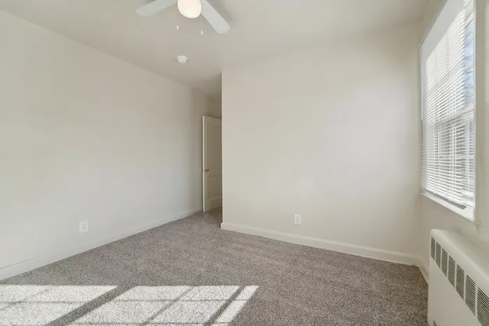 Sunlit bedroom with soft carpet, large window, and neutral walls.