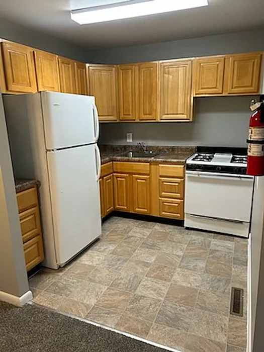 Contemporary kitchen with wooden cabinets, tile flooring, and modern appliances, including a refrigerator and stove.