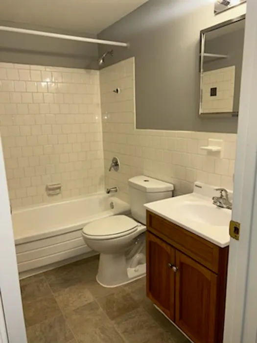 Contemporary bathroom with a white bathtub, toilet, wooden vanity, and tiled walls.