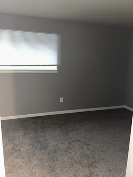 Inviting bedroom with soft grey walls and plush carpeting, featuring natural light from a large window.