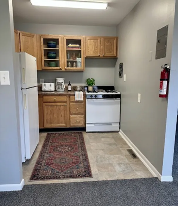 Charming kitchenette with wooden cabinets, a compact stove, refrigerator, and cozy decor for a welcoming touch.