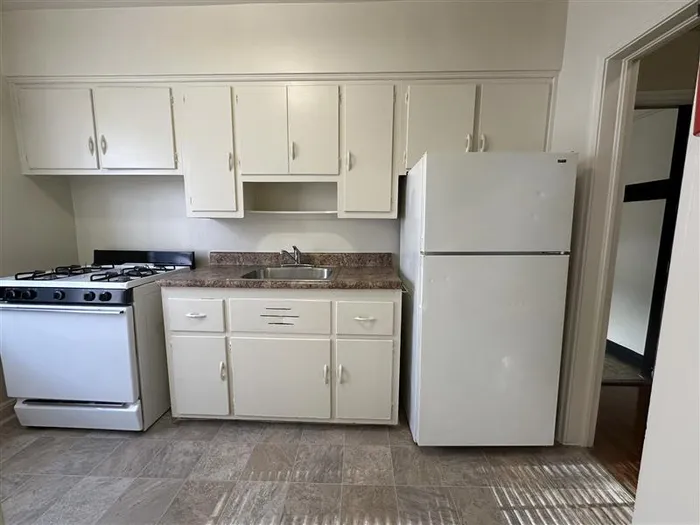 Charming kitchen with classic white cabinetry, a gas stove, and a full-size refrigerator, perfect for culinary enthusiasts.