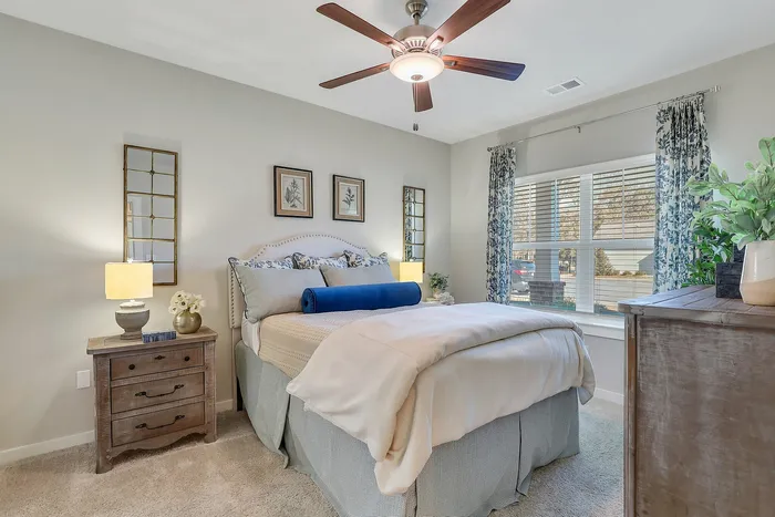 Cozy bedroom with elegant decor, featuring a plush queen-sized bed, stylish blue accents, and natural light from a large window.